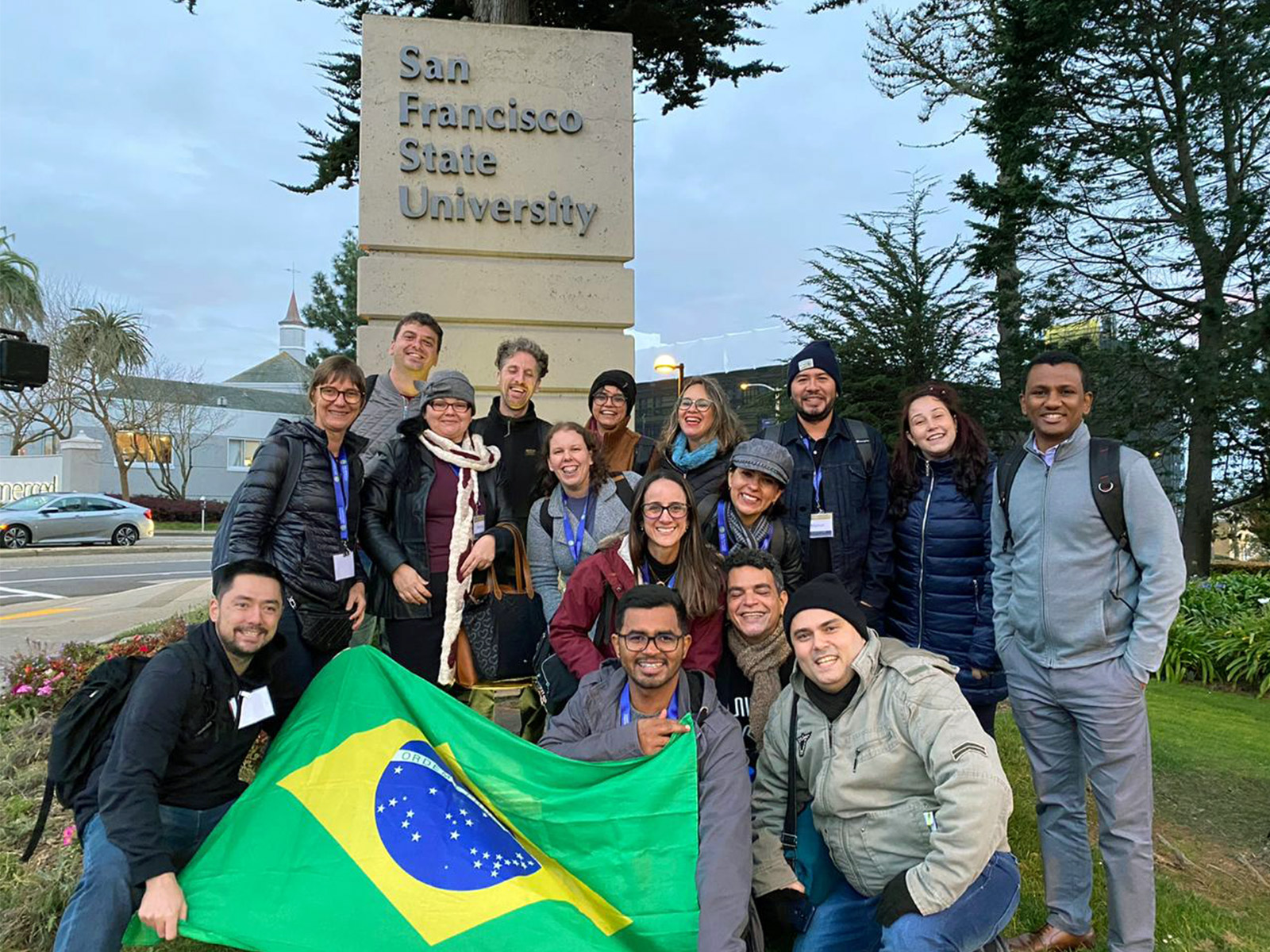 Teacher trainees hold a Brazilian flag in front of the SF State sign